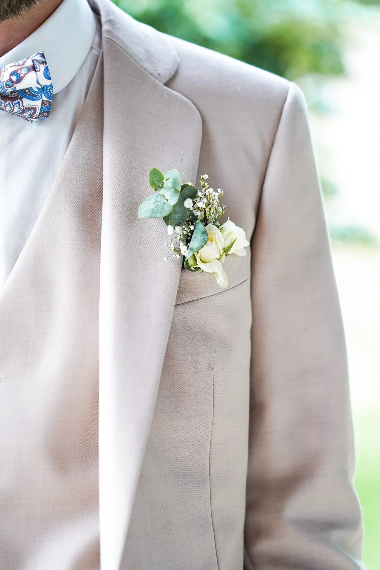 Costume mariage homme beige clair avec une boutonnière verte et blanche.