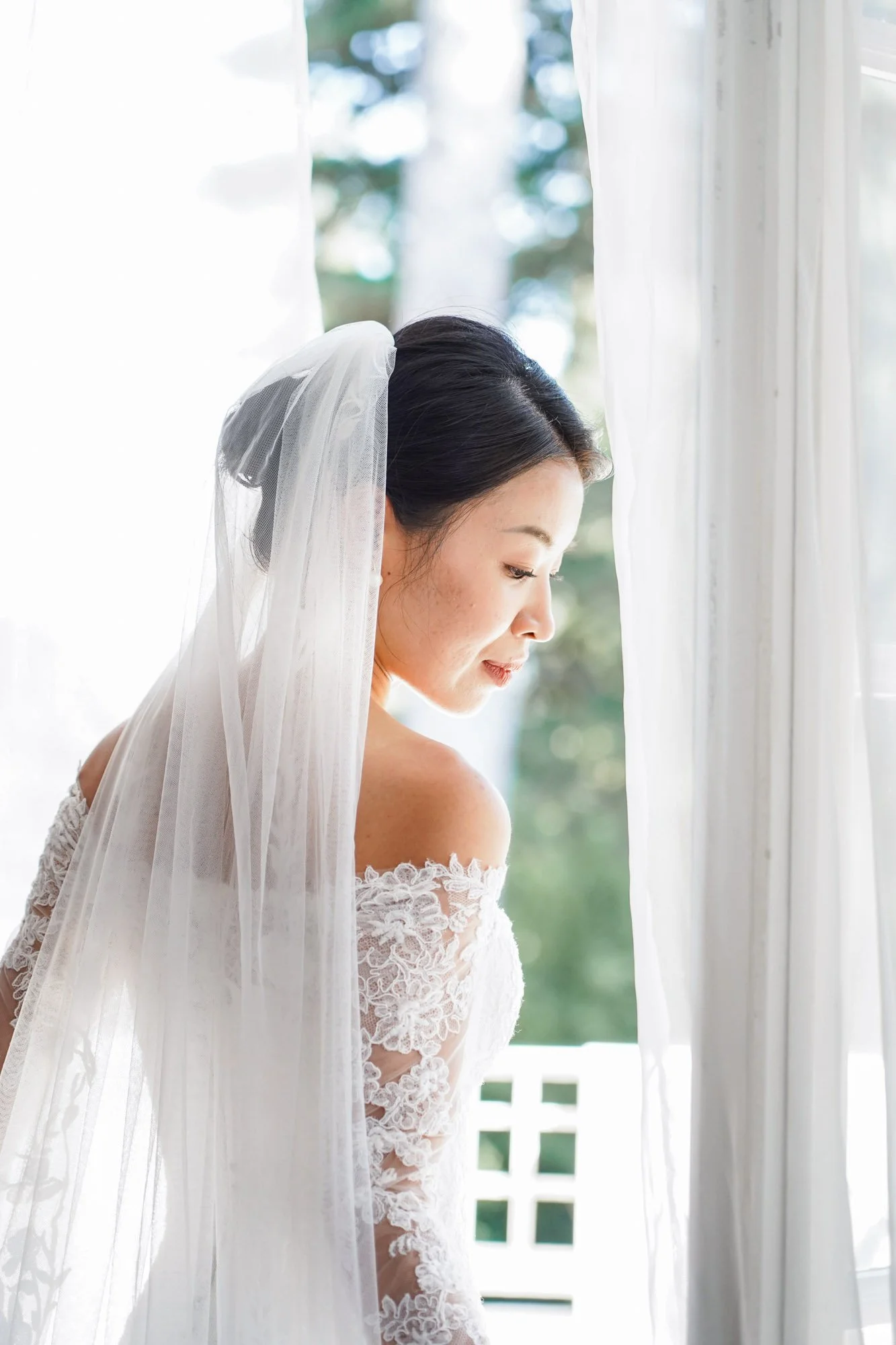 Femme en robe de mariée regardant par la fenêtre, lumière douce.