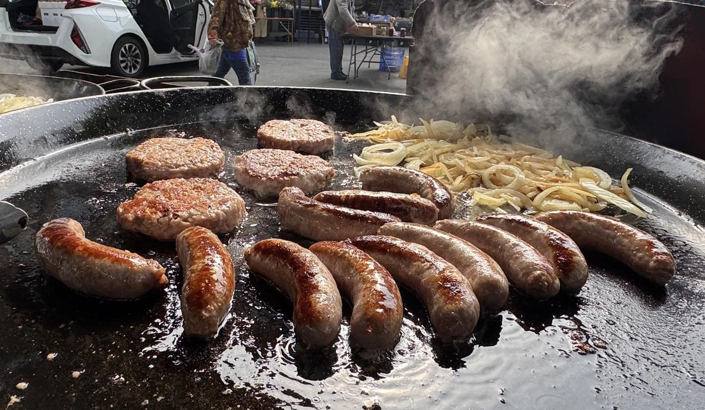 Sausages, patties and onions frying in a large cast iron pan