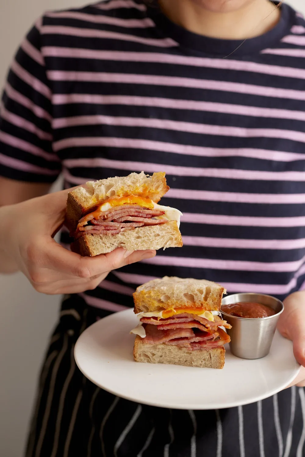 man holding egg and bacon sandwich