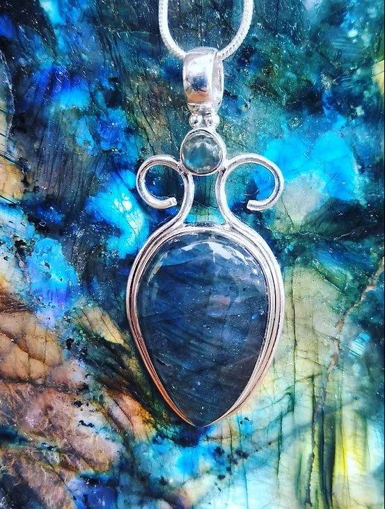 Blue Jeweled silver fleur-de-lis necklace, against a textured blue background