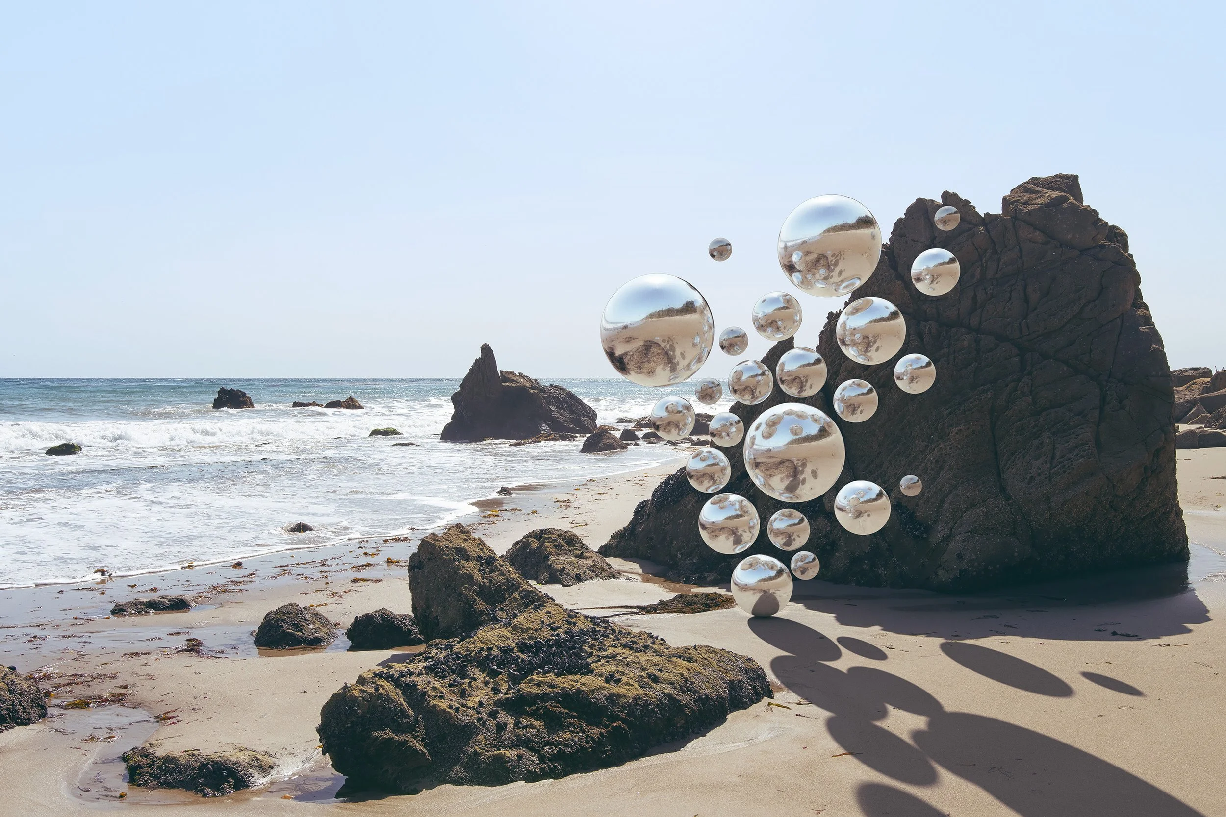 Beach scene with rocks and water, and a double row of floating glass spheres reflecting the surroundings.