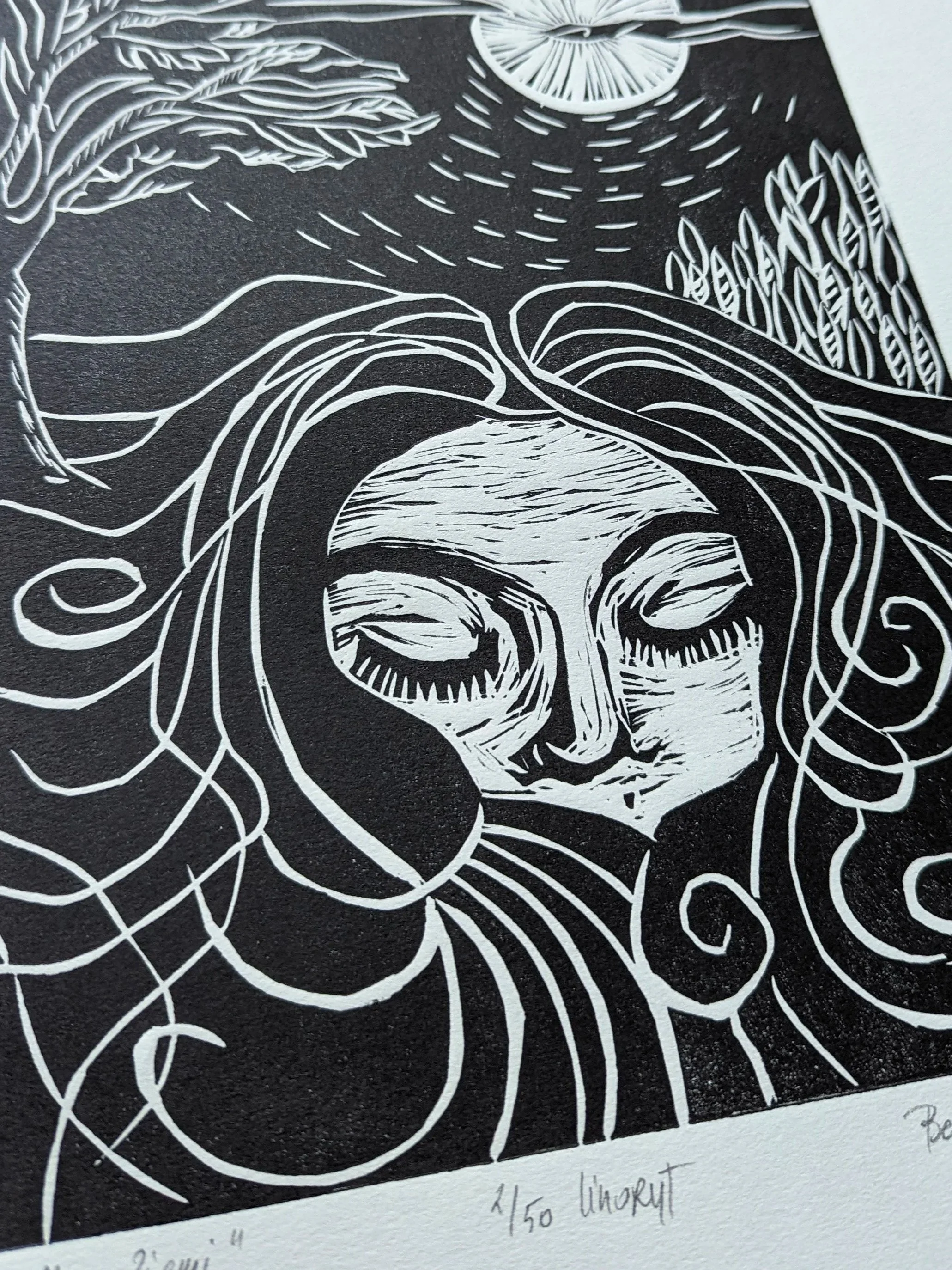 Czarno-biały artystyczny linoryt twarzy kobiety z zamkniętymi oczami, otoczonej falującymi liniami.--
Black and white artistic linocut print of a woman's face with closed eyes, surrounded by flowing lines and abstract patterns.
