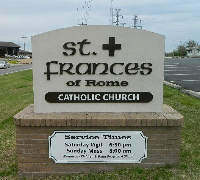 Sign for St. Frances of Rome Catholic Church displaying service times for Saturday vigil at 6:30 pm and Sunday mass at 8:00 am.
