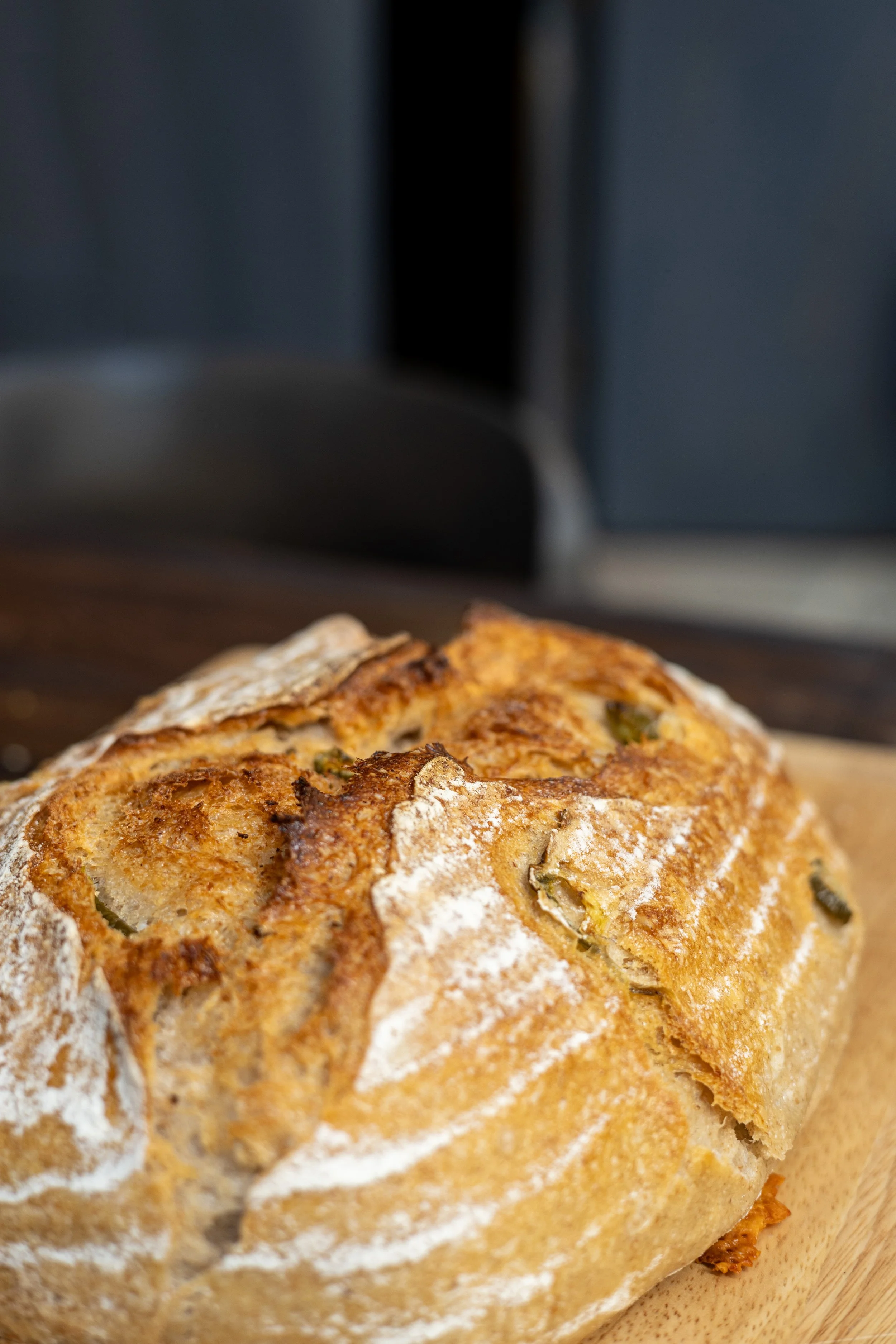 Close-up of a rustic loaf of bread with a golden-brown crust, dusted with flour, resting on a wooden surface.