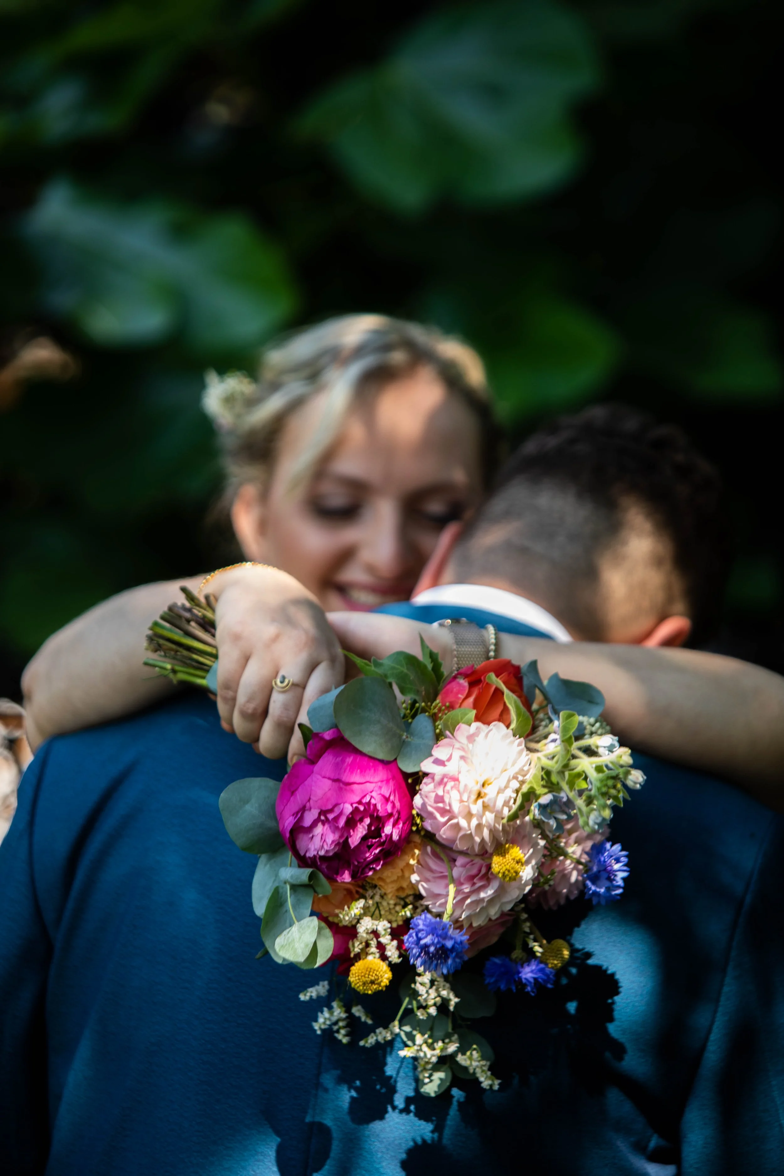 Un couple s'enlace lors d'une cérémonie de mariage, avec un bouquet de fleurs colorées.