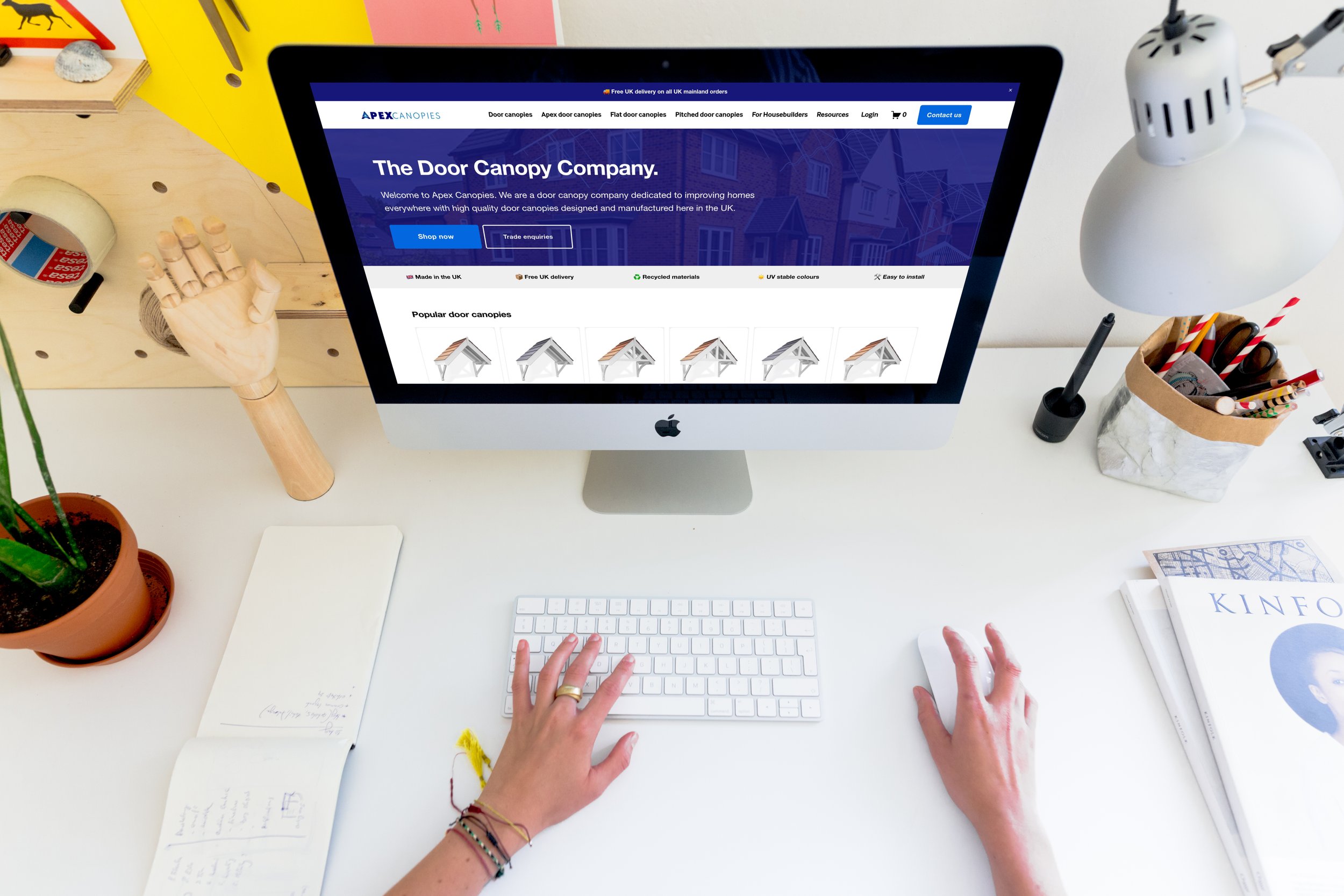 Computer screen displaying the homepage of Apex Canopies, a door canopy company, with a person typing on a white keyboard.
