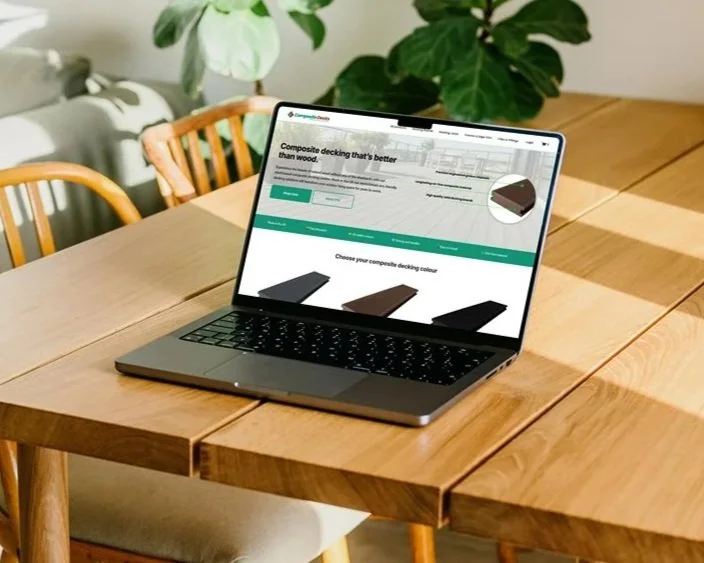 Laptop on wooden dining table showing a website about composite decking options.