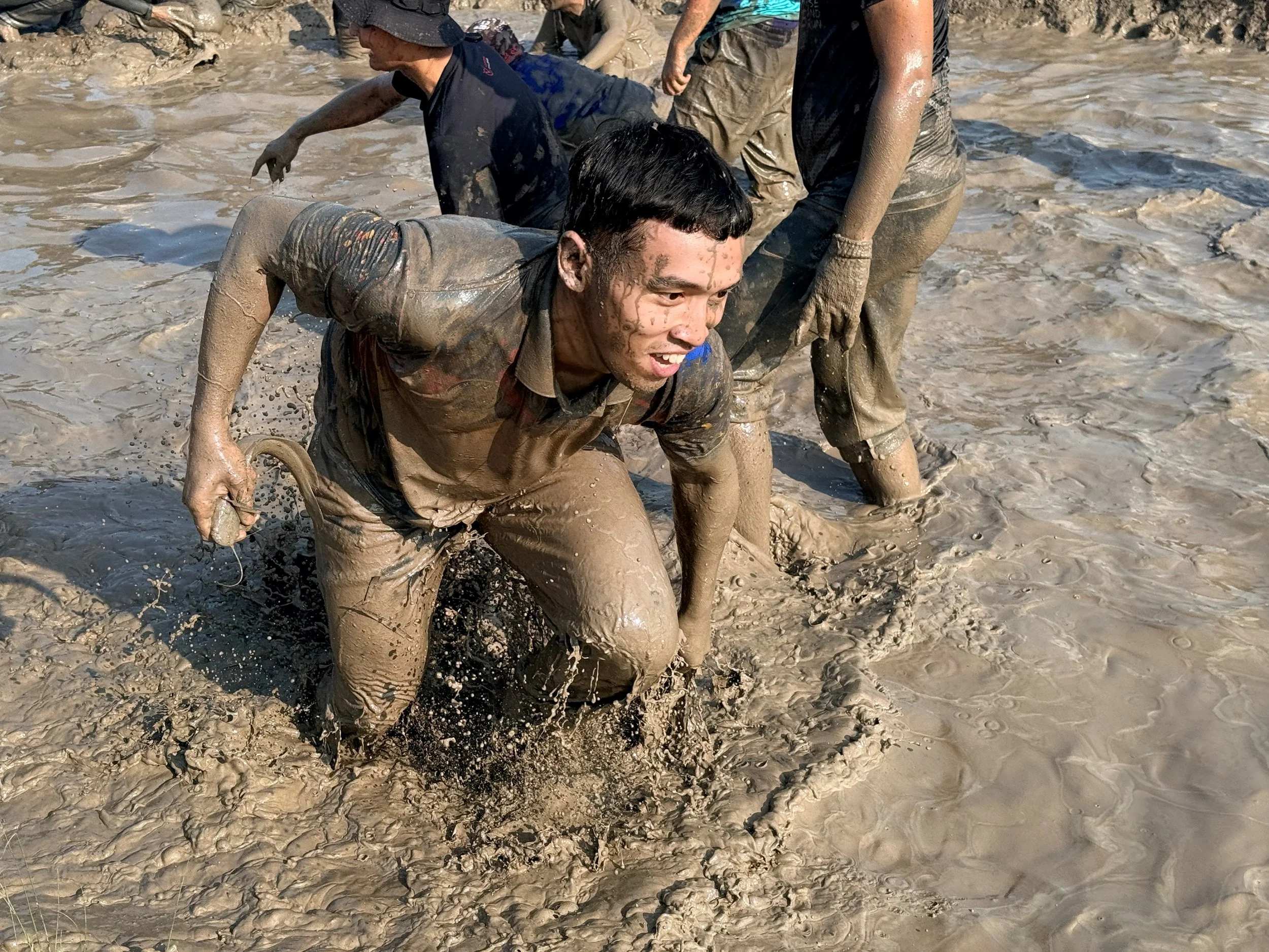 Group of people covered in mud, crawling through muddy terrain during outdoor activity.