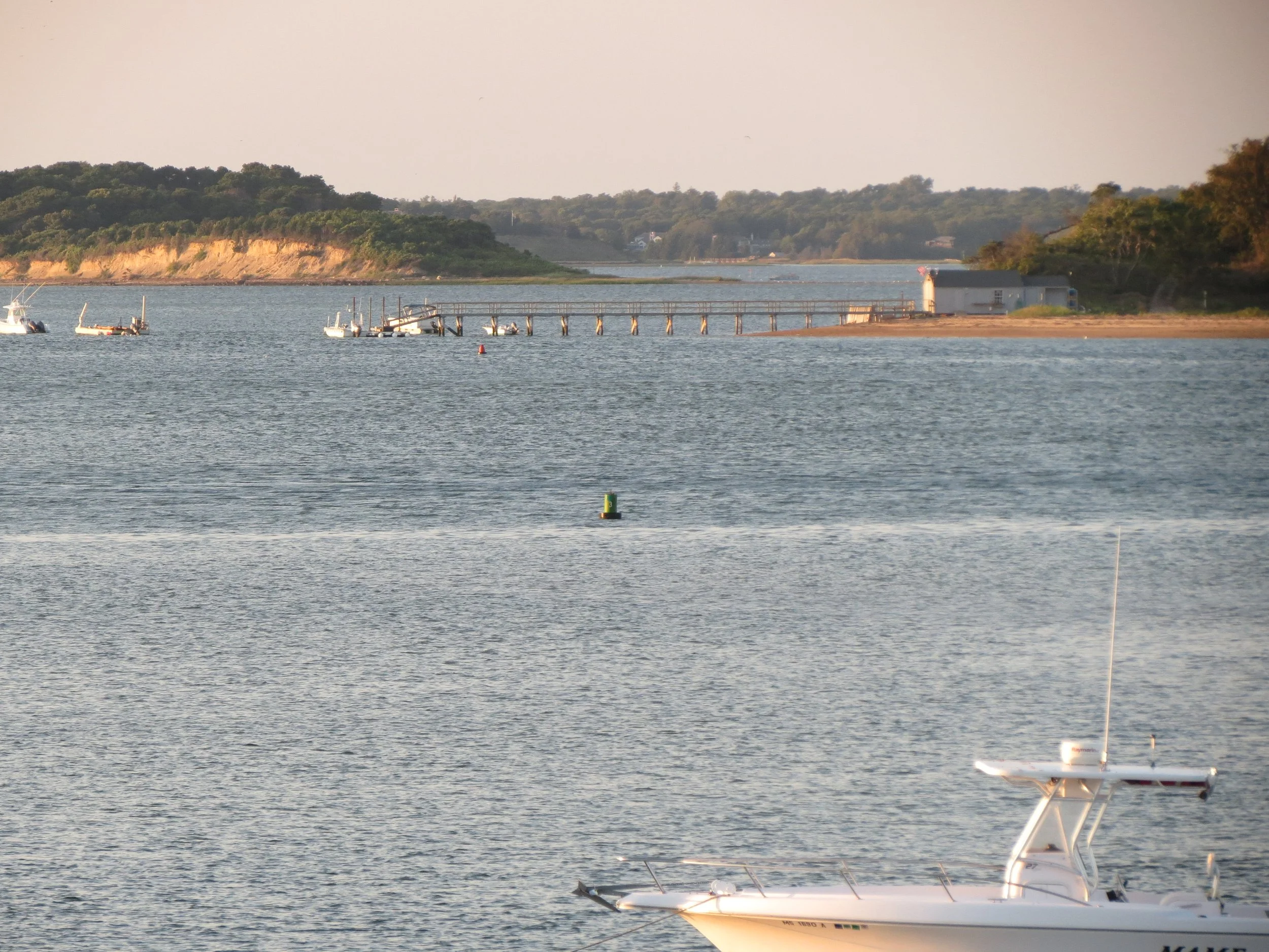 A peaceful lakeside scene with boats docked and a pier extending into the water, with trees and hills in the background during sunset.