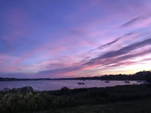 Sunset over a river with boats and-green shoreline.
