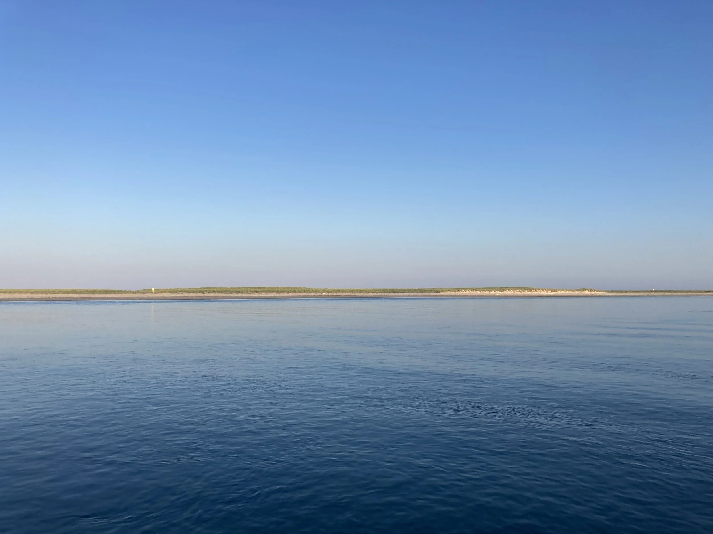 Calm ocean with a distant shoreline and a clear blue sky.