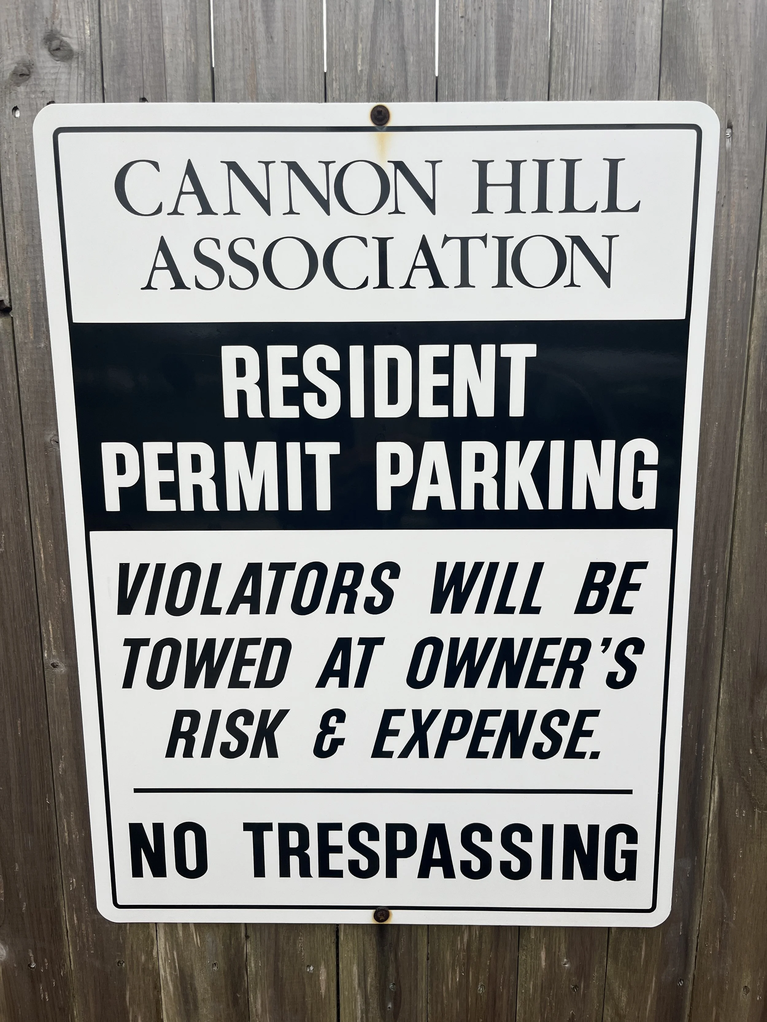A warning sign for Cannon Hill Association indicating resident permit parking, with a warning that violators will be towed at owner’s risk and expense and that no trespassing is allowed.