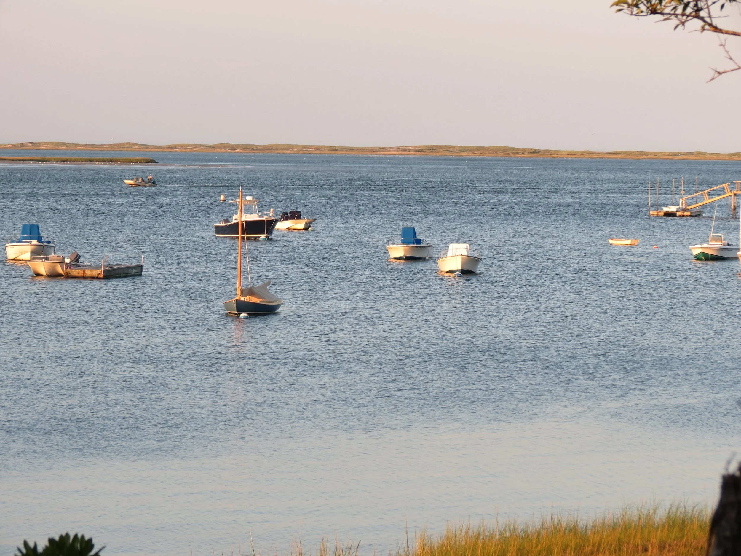 Boats anchored in a calm body of water, with a distant shoreline and a clear sky.