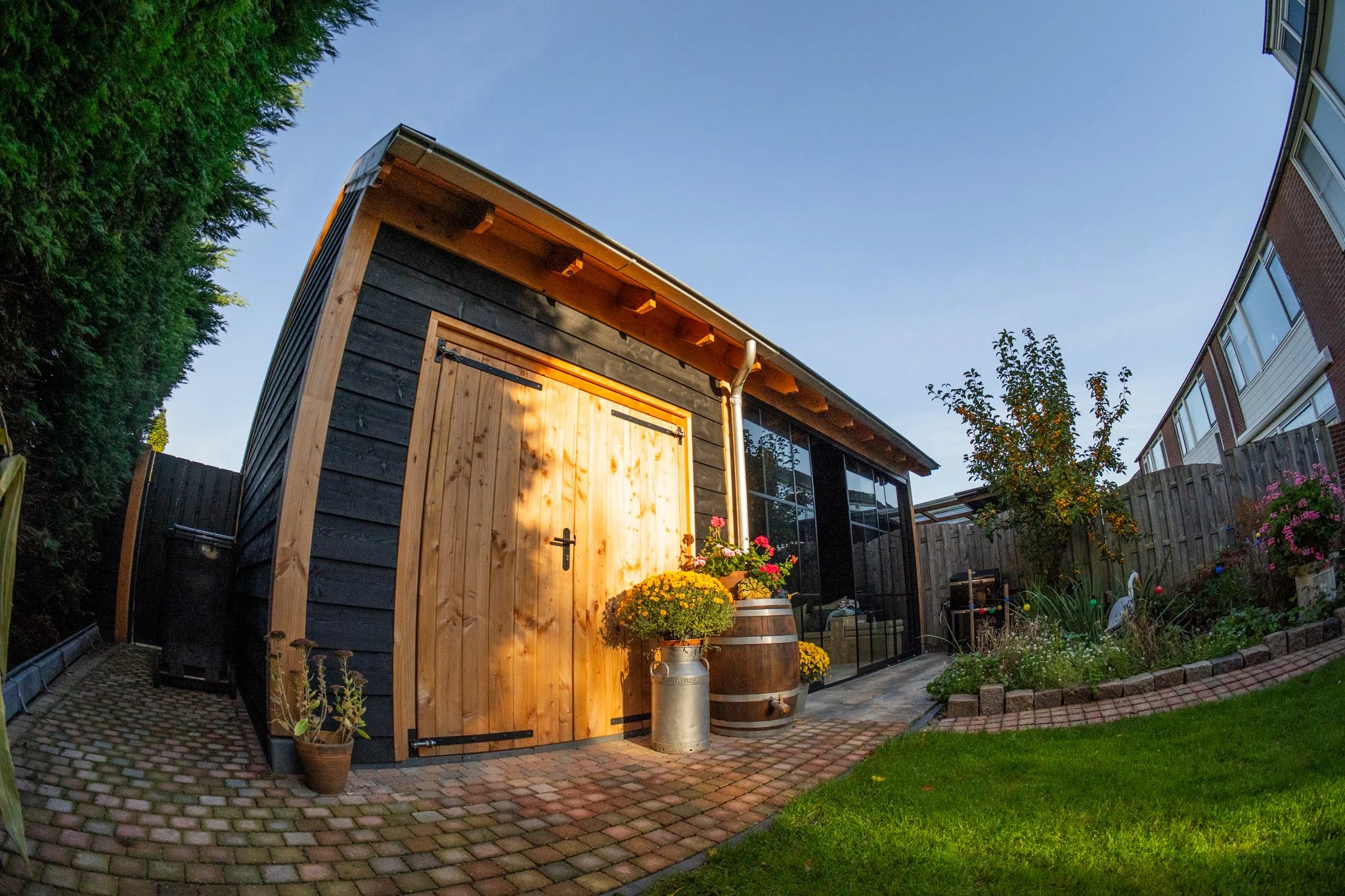 Een tuin met een schuur, versieringen en bloemen, onder een heldere blauwe hemel.