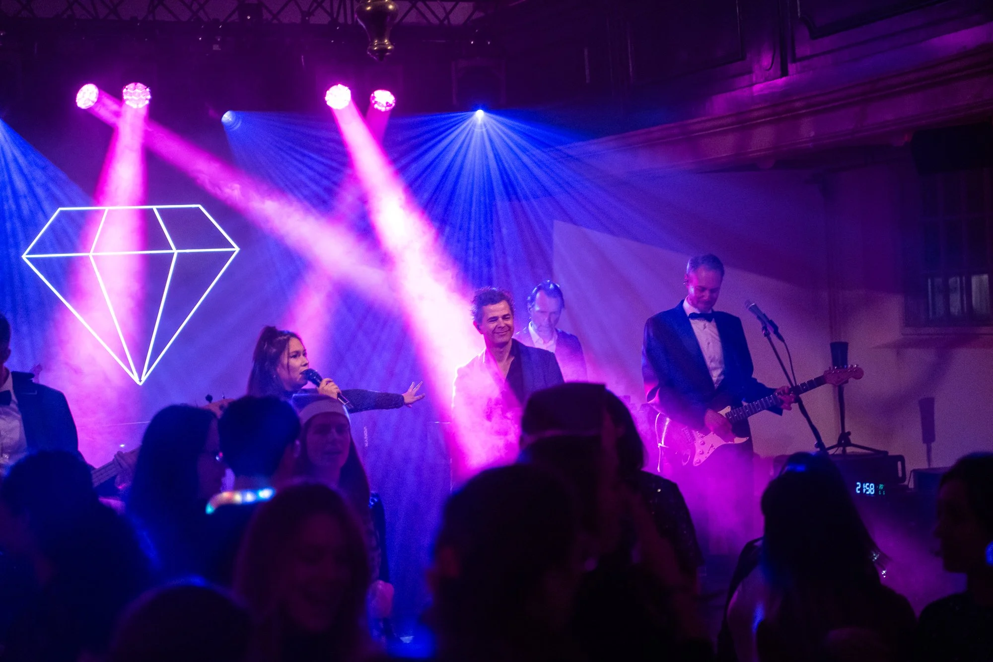 Groep muzikanten op een podium met neon licht en rook effect, bij een feest of concert.