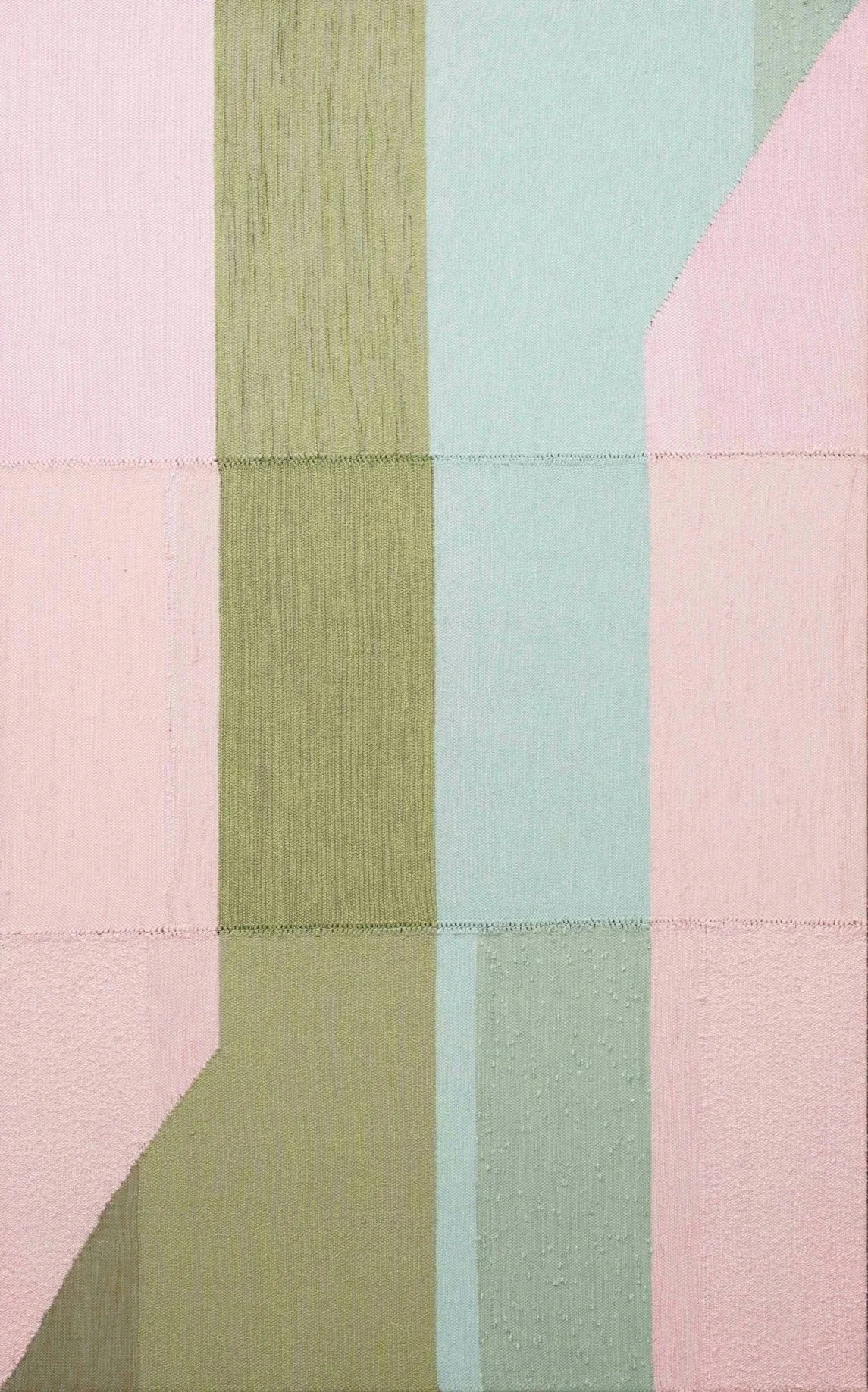 A close-up of a textured fabric with pastel-colored geometric shapes, including pink, olive green, light blue, and gray, separated by visible stitching.