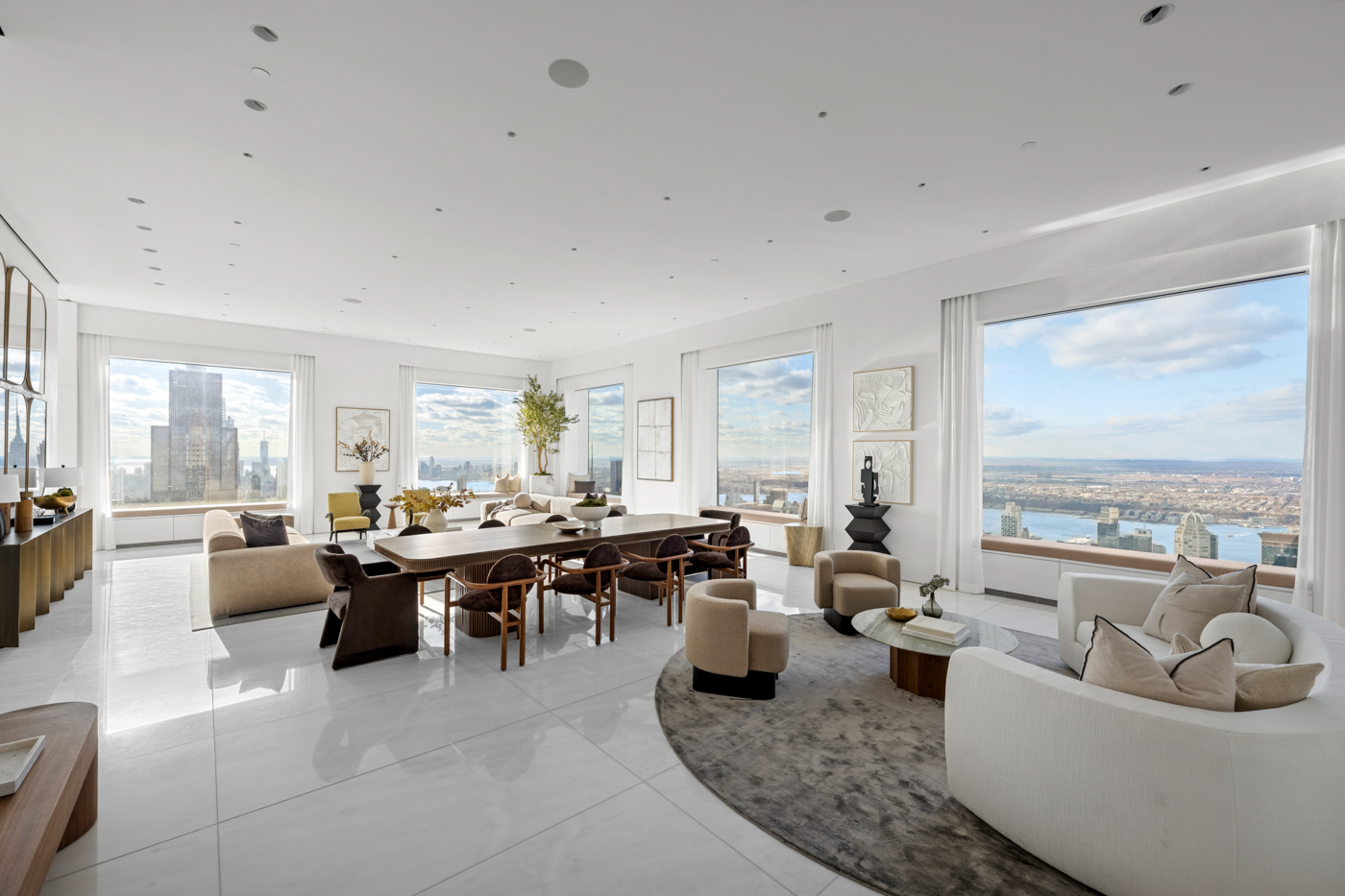 Bright and spacious living room with large windows showing a city skyline and river, decorated with modern furniture, artwork, and potted plants.