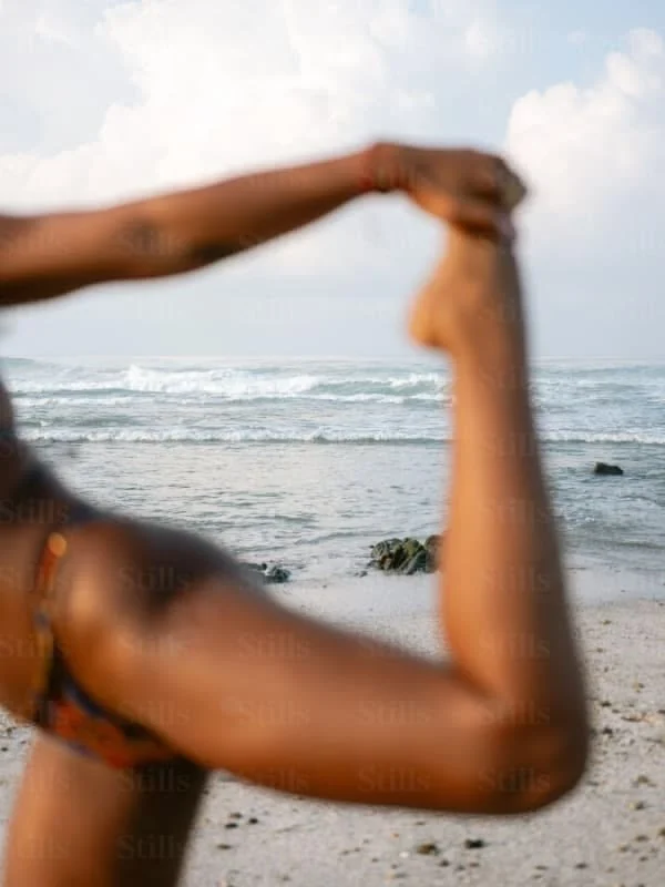 Blurred image of a person's arm flexing at the beach, with ocean waves and rocks in the background.