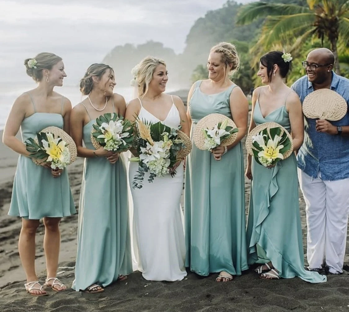 A tropical destination wedding party with bridesmaids in light blue dresses on a lush beach, styled by international bridal artist Cecilia Acquaroli.