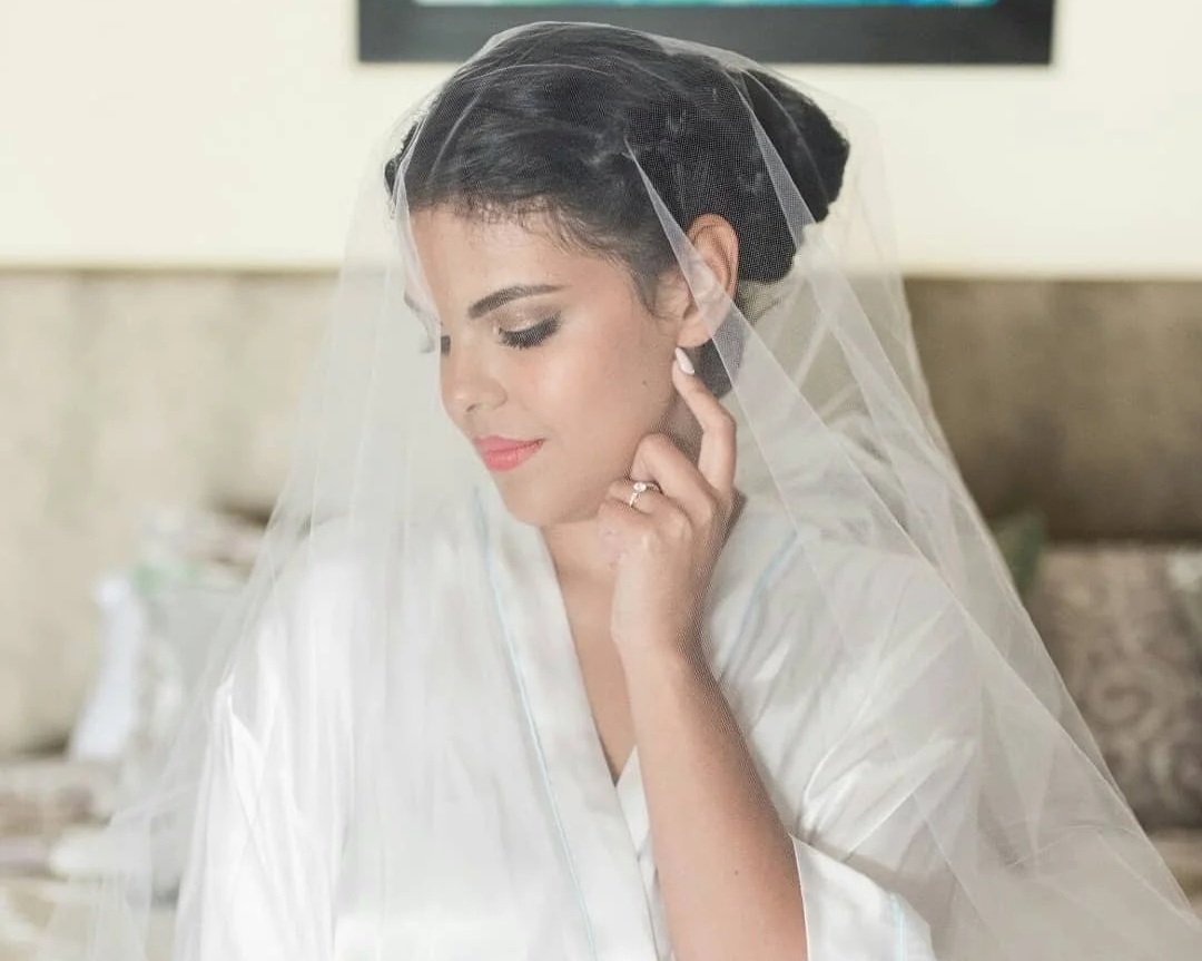 Close-up of a bride with a veil, looking down and touching her ear gently.