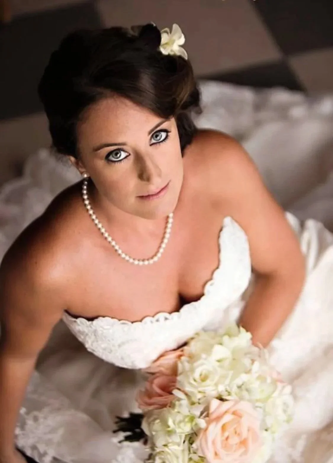 A timeless bridal look for a woman in a wedding dress holding a bouquet of white and pink flowers, looking up at the camera.