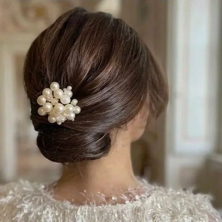 A woman with brown hair styled in an elegant updo, decorated with a cluster of white pearl hair accessories.