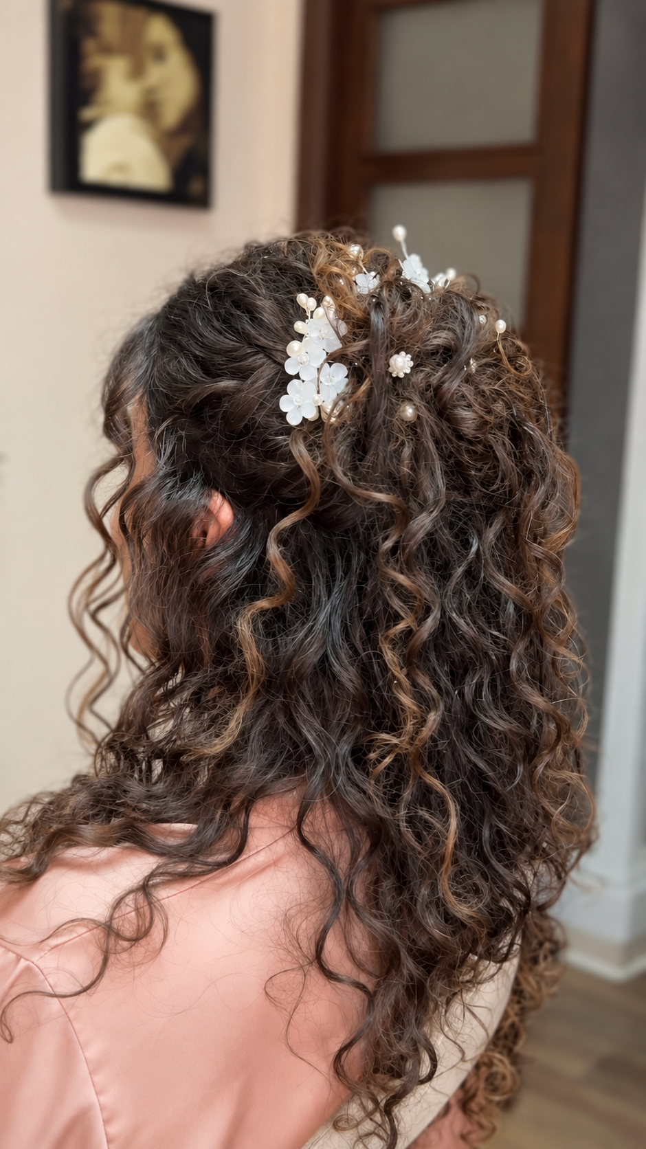 Close-up of a woman's curly hair styled with white floral hair accessories, seen from the back.