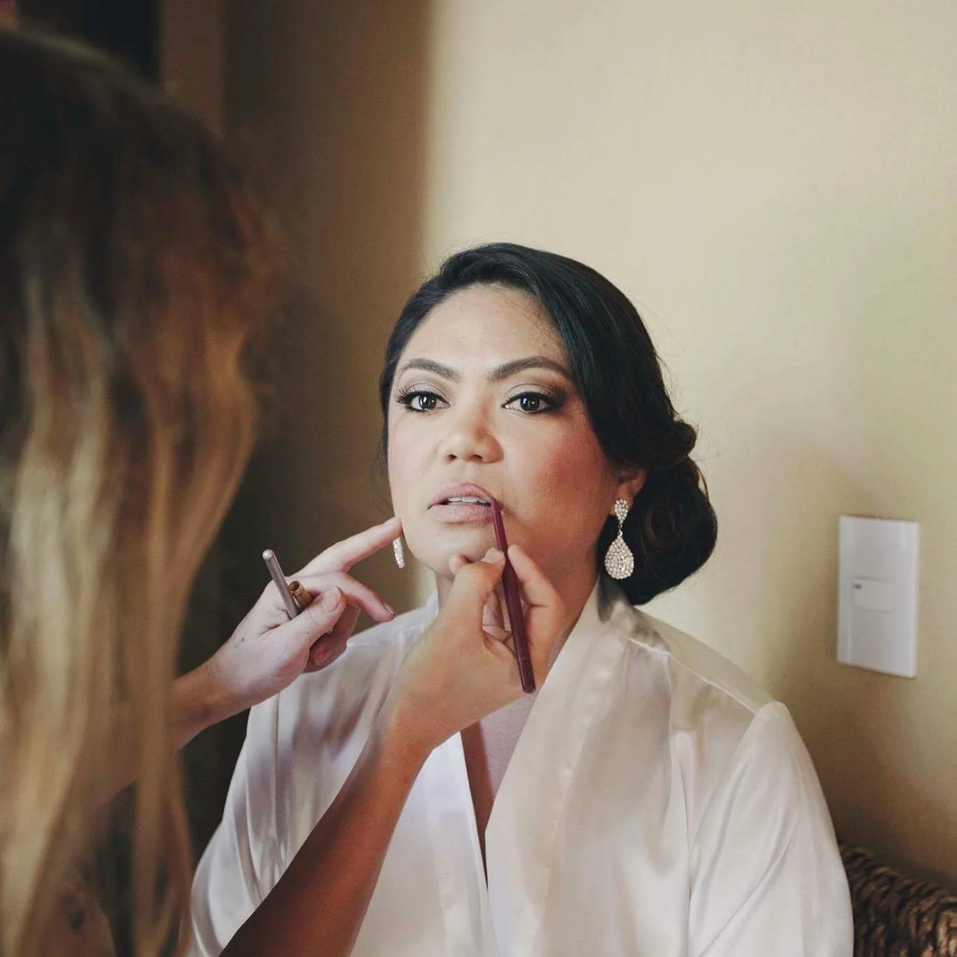 Woman in white robe having her makeup applied by makeup artist.