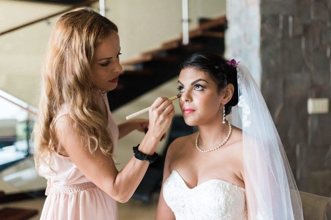A focused and calm bridal makeup session in Rome, showcasing meticulous artistry and a sophisticated wedding hair design .The bride is wearing a white wedding dress, pearl necklace, earrings, and a veil, with dark hair styled back.