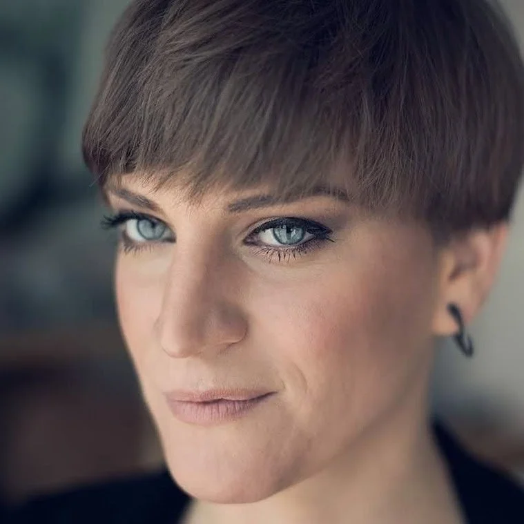 Close-up of a woman with short brown hair and blue eyes looking slightly to the side.