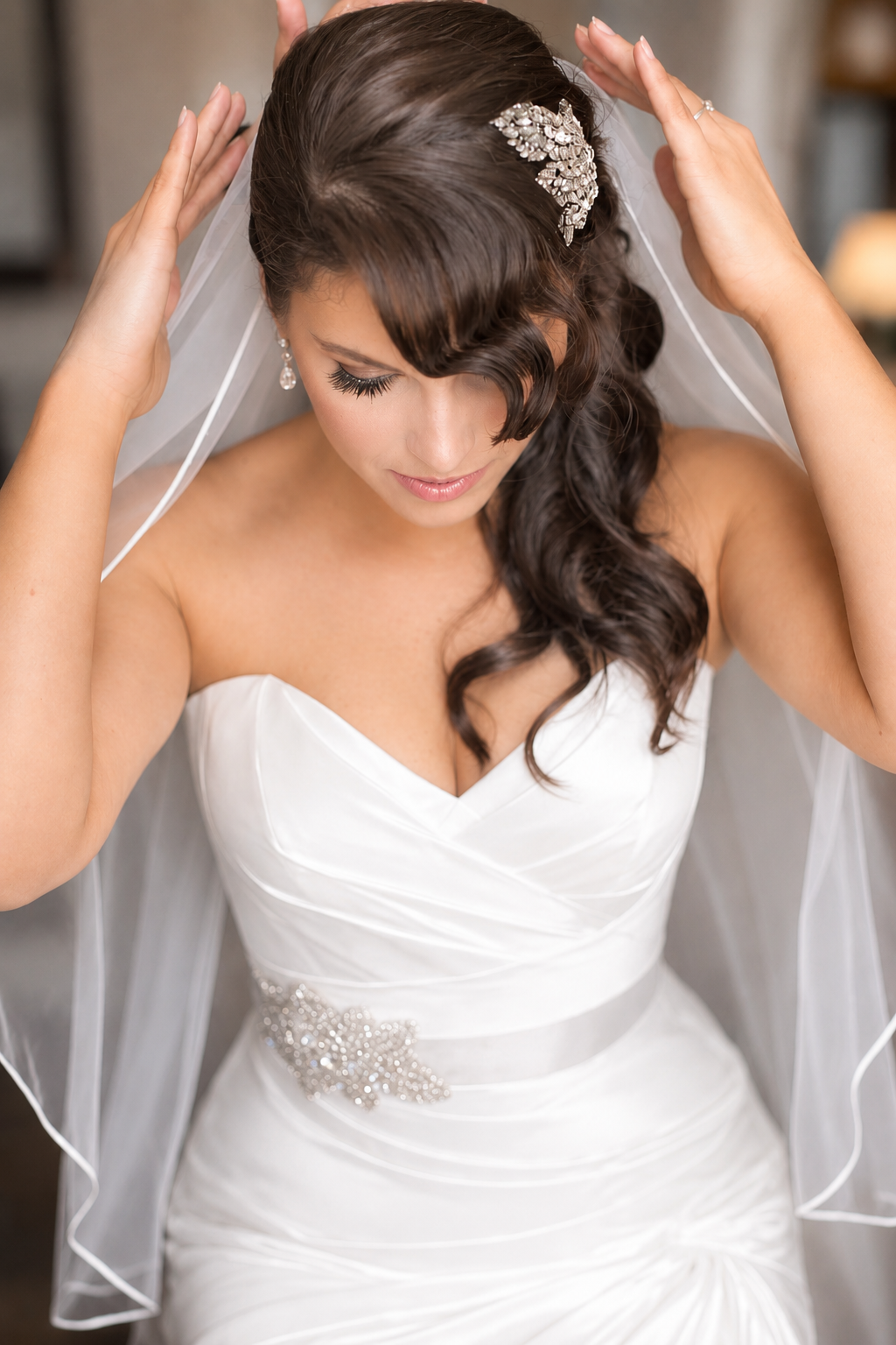 A bride with dark brown, wavy hair and a jeweled hair accessory, adjusting her veil before a wedding. Styled by Cecilia Acquaroli