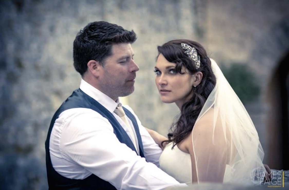 Featuring a bride styled by Cecilia Acquaroli, and her groom in wedding attire close together, outdoors with a stone wall background of a castle in Venice