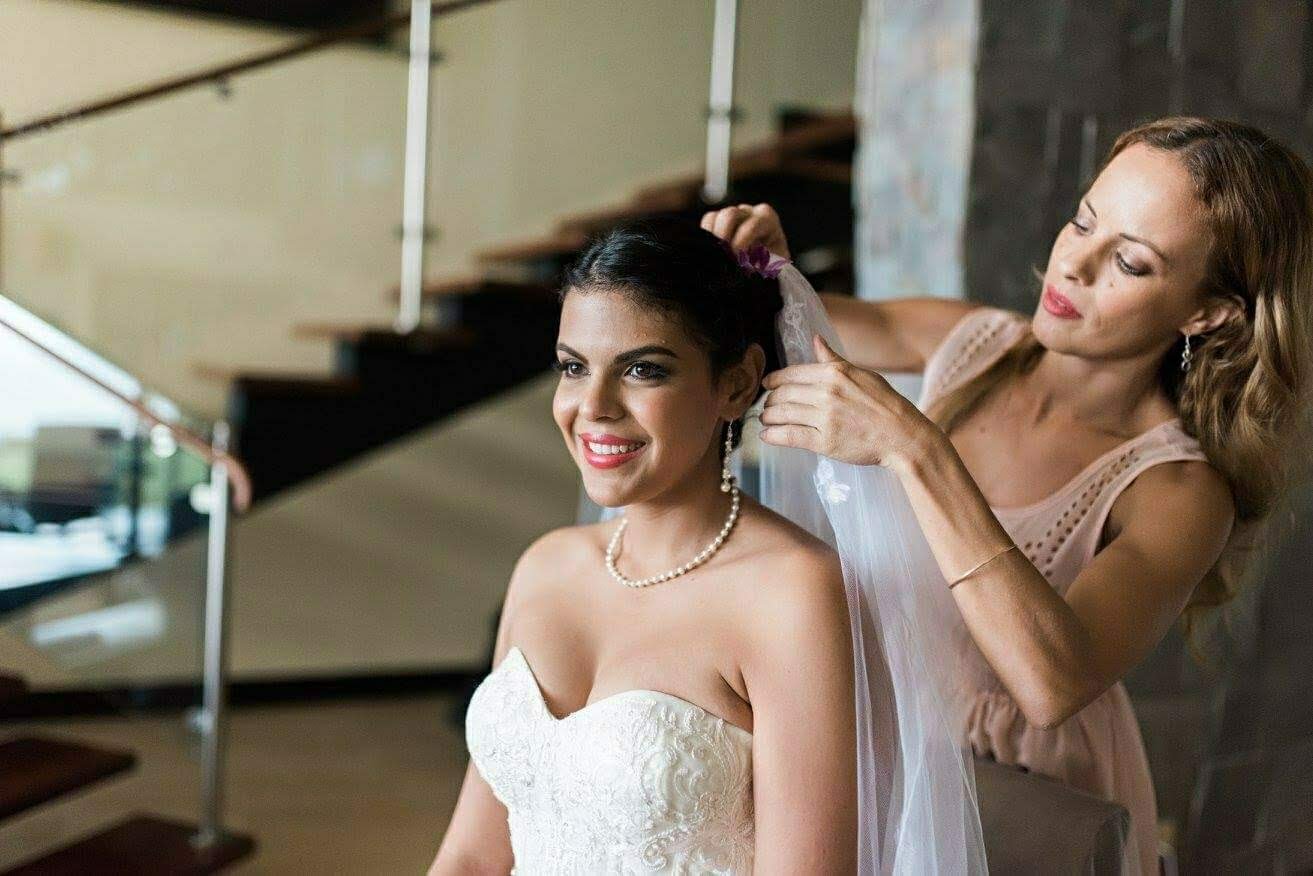 A bride in a strapless wedding dress, smiling as her bridal stylist Cecilia Acquaroli adjusts her veil.