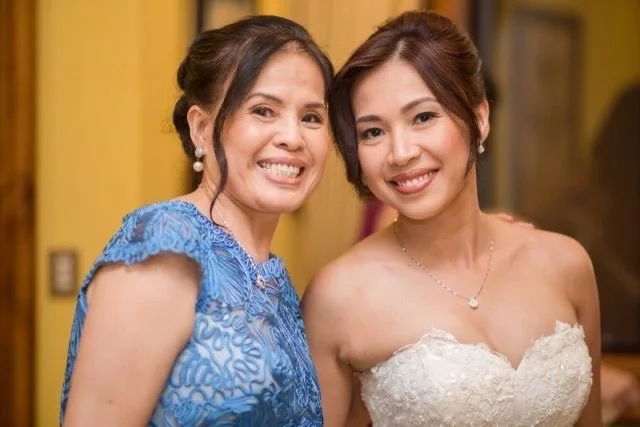 A bridal mother and daughter moment, as they're smiling and posing for a photo after the finished llook. 