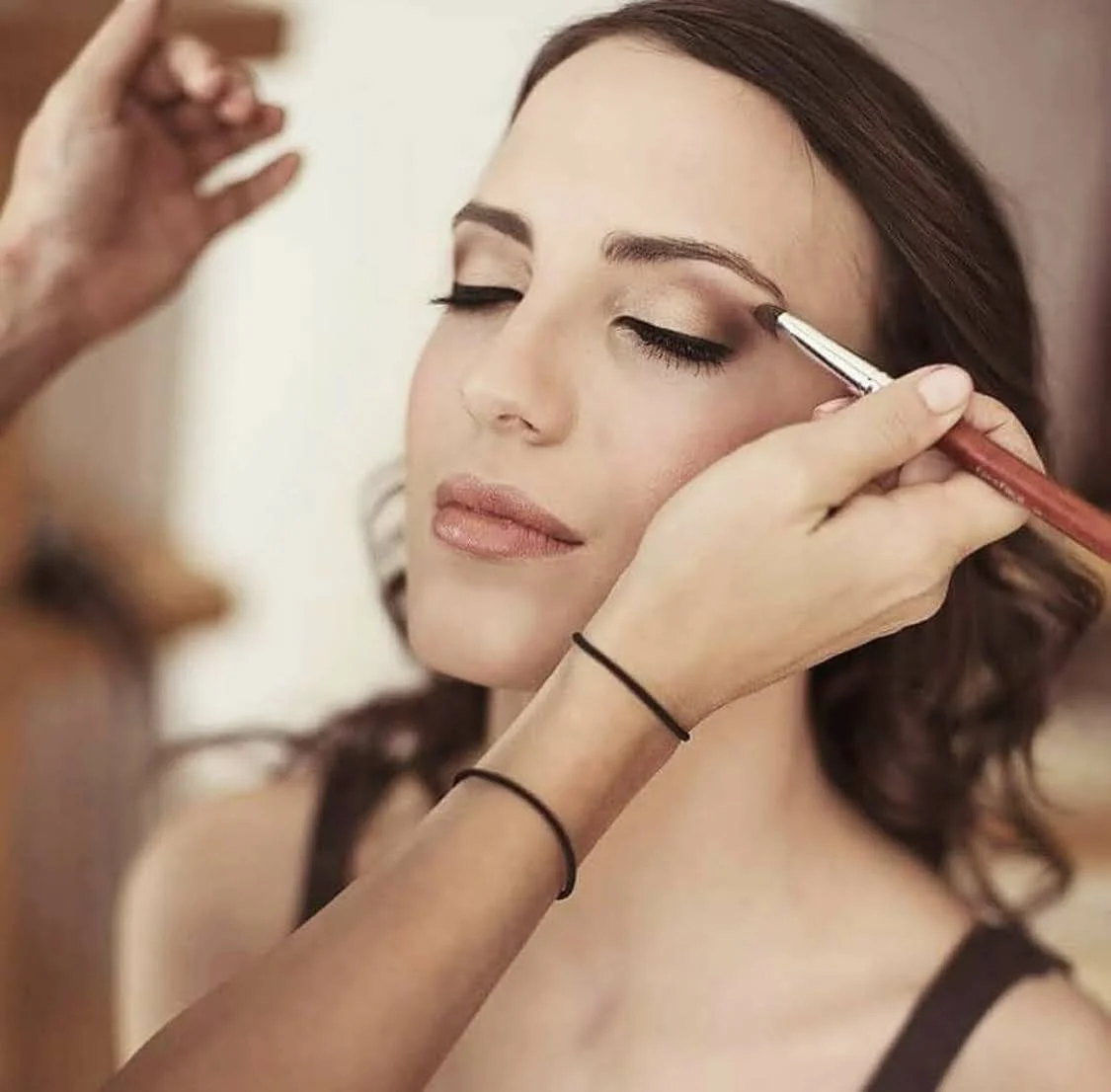 Close-up of a wedding stylist performing a final makeup touch-up on a bride, emphasizing luminous skin and a classic look.