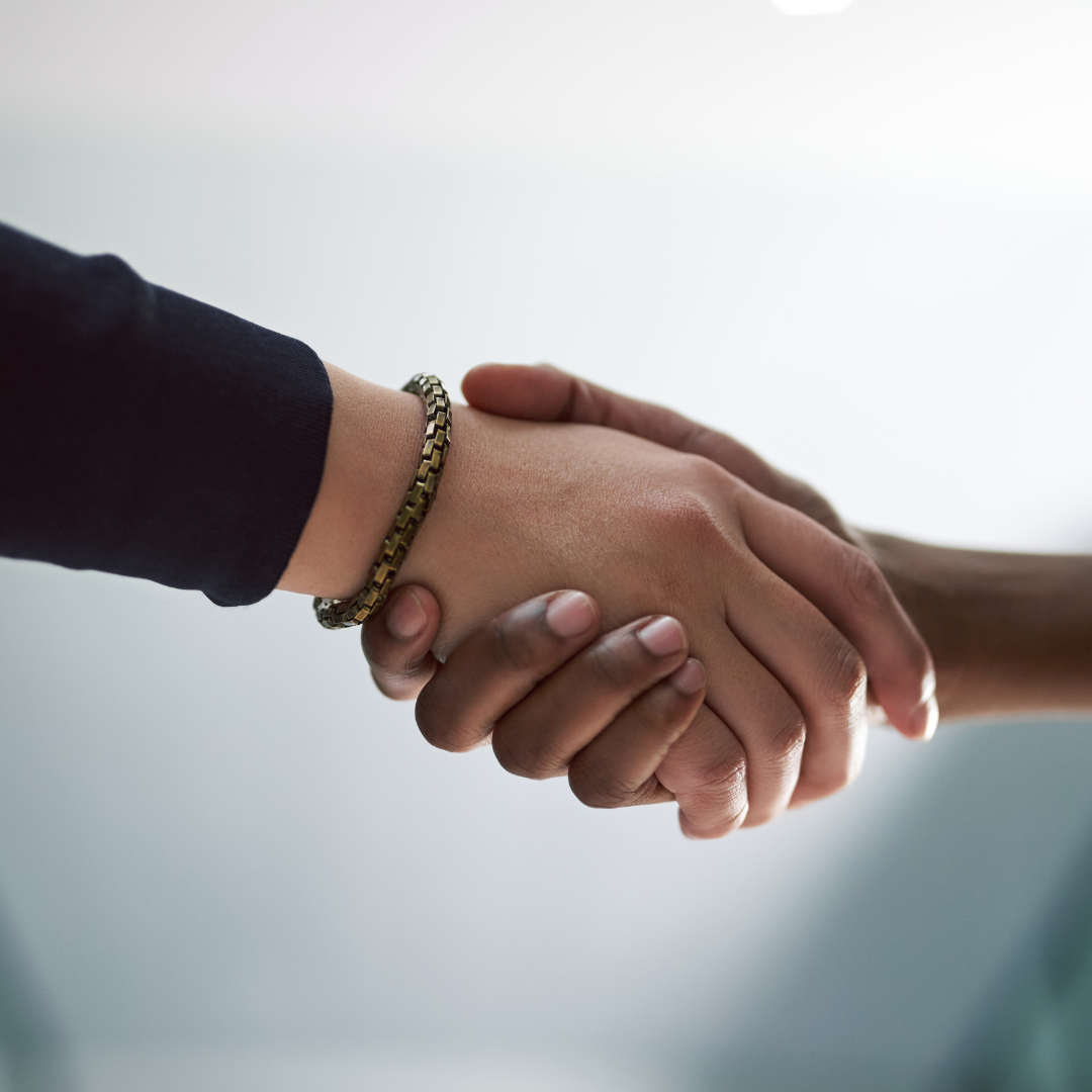 Close-up of two hands shaking, one wearing a black sleeve and a gold bracelet.