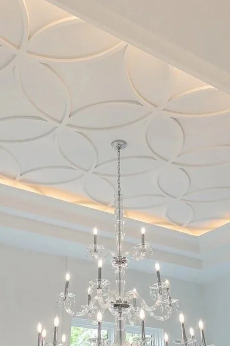 A decorative white ceiling with circular patterns and a crystal chandelier hanging from the center.