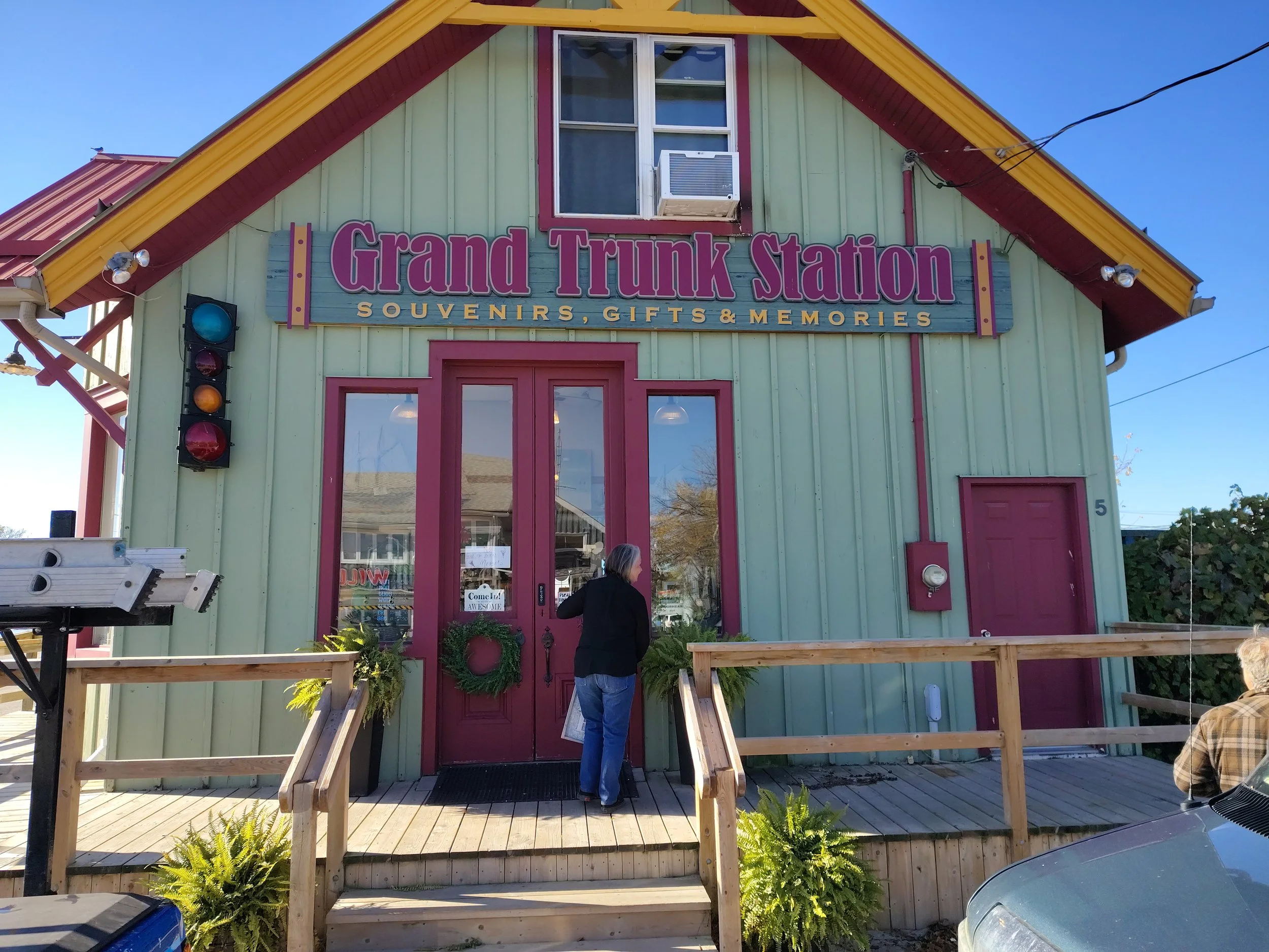 Colorful building with a sign reading 'Grand Trunk Station' and 'Souvenirs, Gifts & Memories.' Someone is standing at the door, and a traffic light with blue, yellow, and red lights is on the left side of the building.