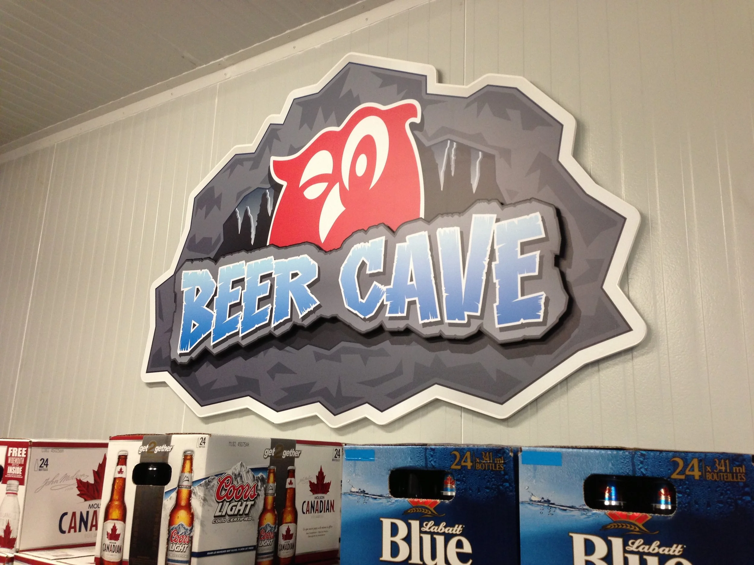 A sign reading 'Beer Cave' with a red bear paw illustration above it, mounted on a wall in a store.