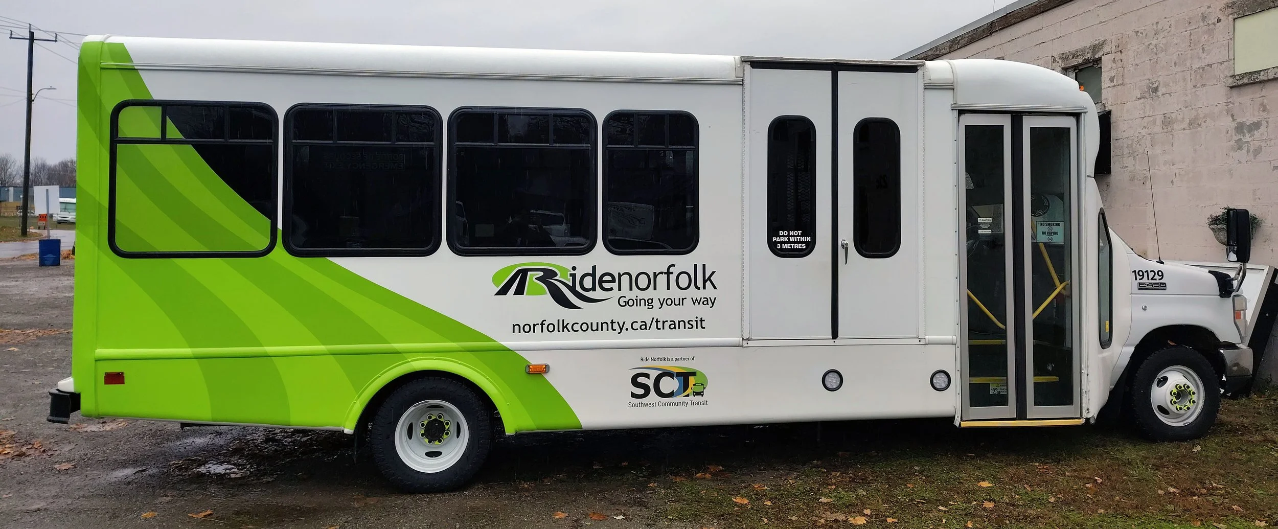 Green and white transit bus with Norfolk County branding, parked outdoors on a cloudy day.