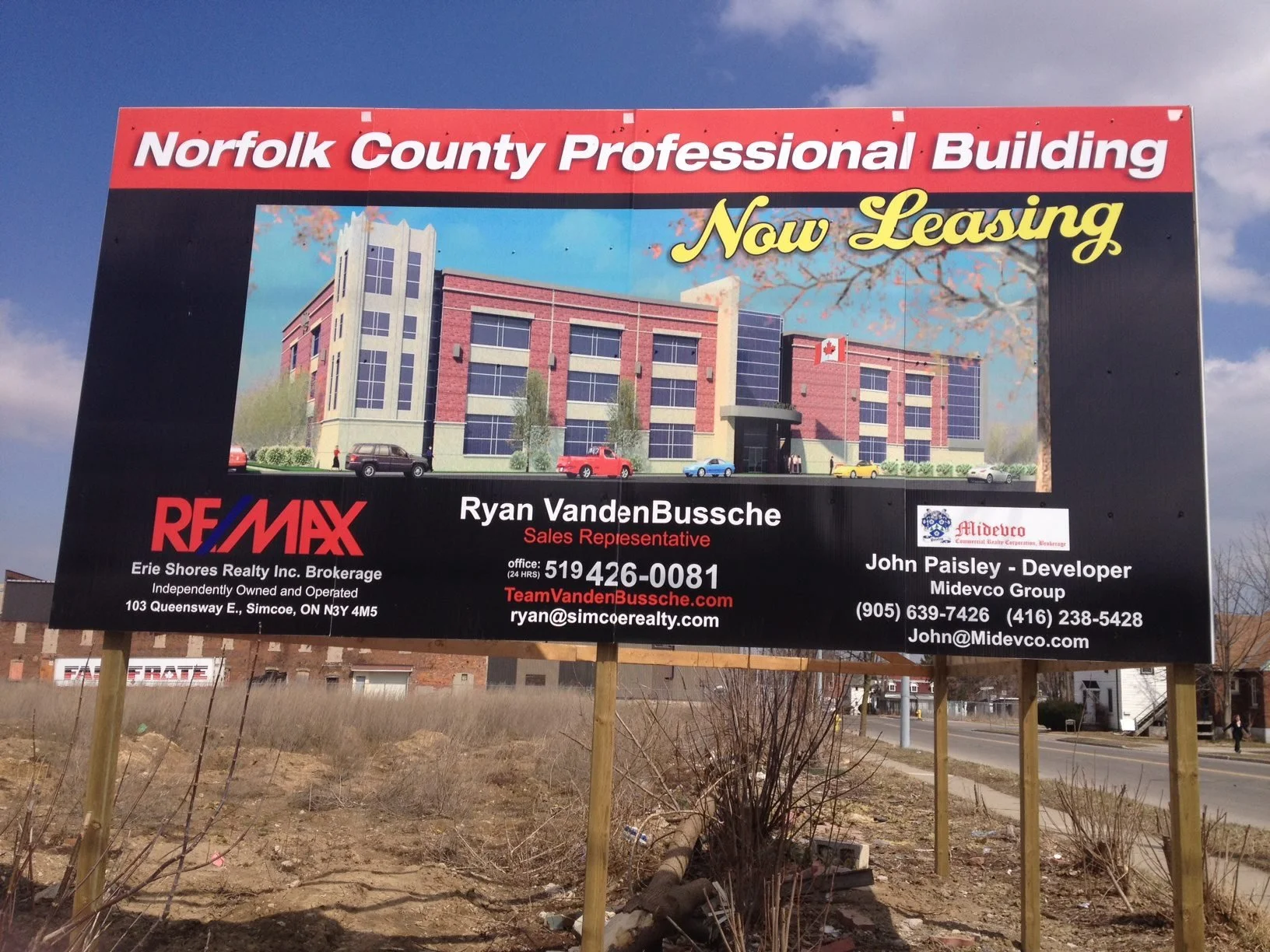 A large outdoor billboard advertising a new commercial building for lease in Norfolk County, with a digital rendering of the building, real estate agent and developer contact information, and real estate company logos.