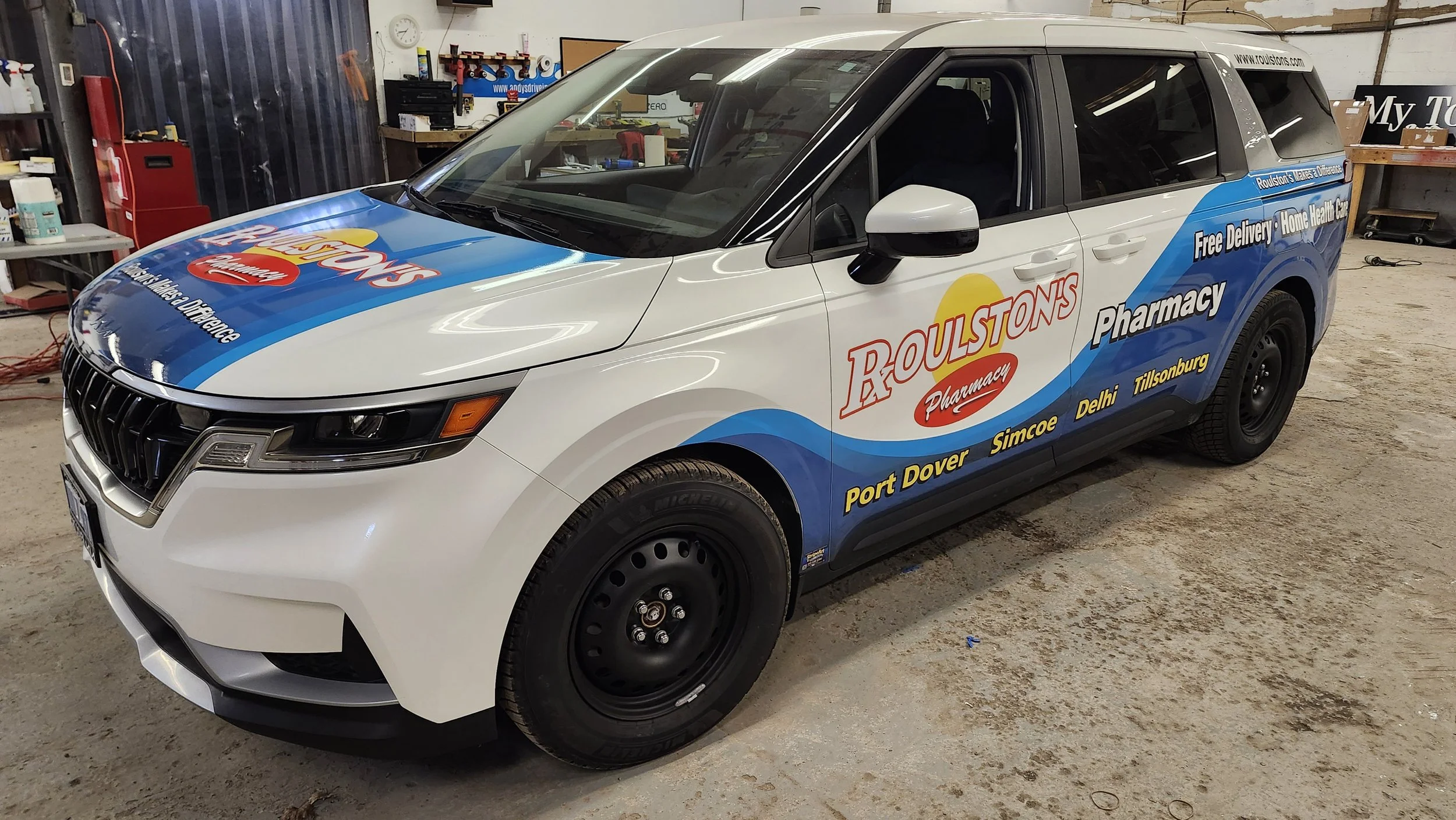 A vehicle with Roulstons Pharmacy branding, white with blue and red decals, parked inside a garage or workshop.