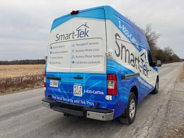 A blue and white service van for Smart-Tek Security and Tek Pros parked on a rural road, advertising security and locksmith services.