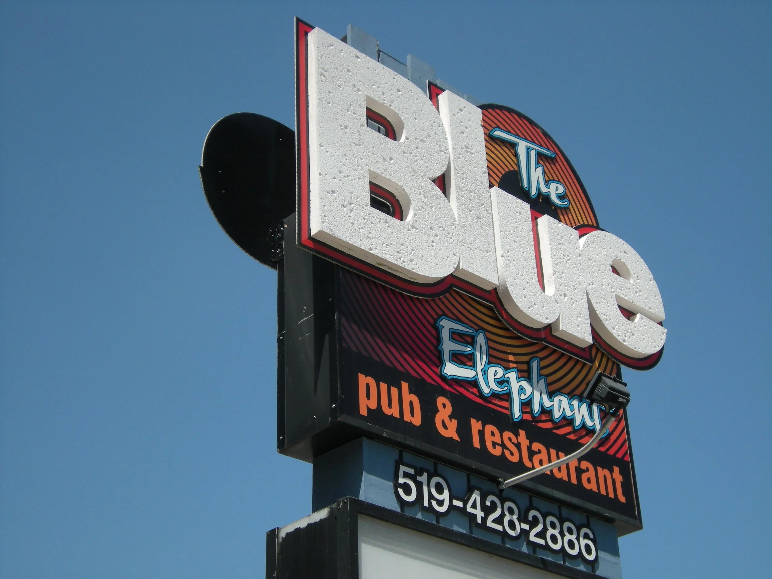 Sign for 'The Blue Elephant' pub and restaurant with phone number 519-428-2886, against a clear blue sky.