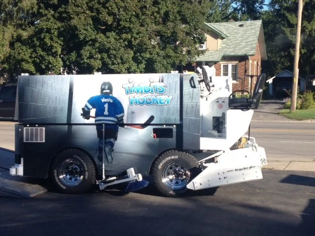 Street cleaning machine painted with a hockey theme, featuring a hockey player in a blue jersey with the number 1 and the words "Timbi's Hockey."