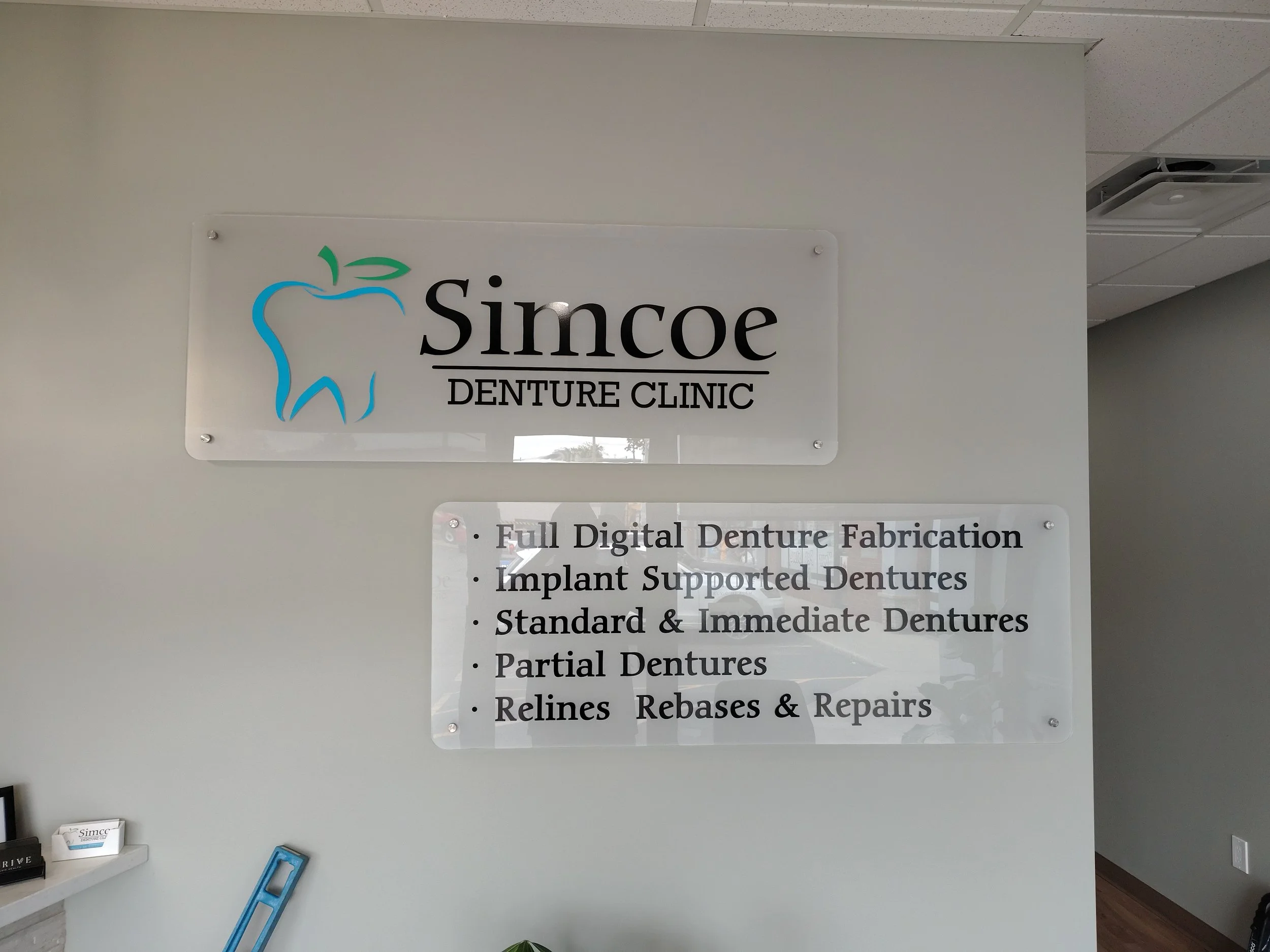 Sign for Simcoe Denture Clinic with logo of a tooth and list of services like full digital denture fabrication, implant supported dentures, standard and immediate dentures, partial dentures, relines, rebases, and repairs.