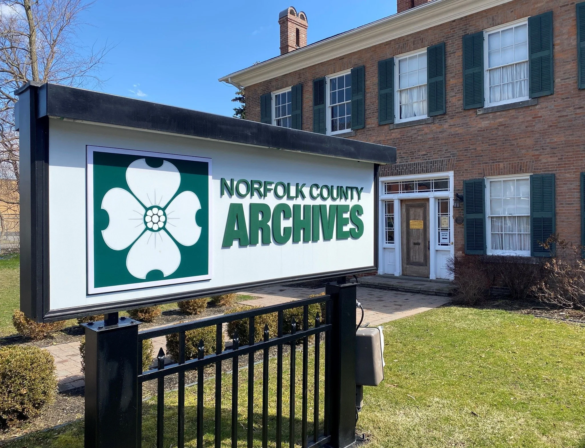 Sign for Norfolk County Archives in front of a brick building with green shutters and multiple windows.