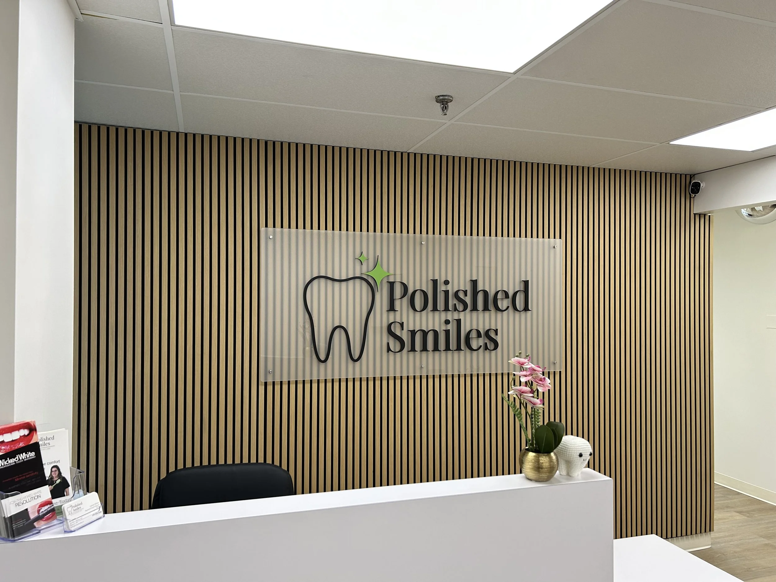 Dental office reception area with a sign reading 'Polished Smiles', a potted orchid, and dental brochures on the counter.
