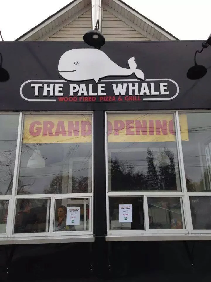 The exterior of a restaurant called 'The Pale Whale' which offers wood fired pizza and grill, with a sign indicating it has a grand opening in Penn.